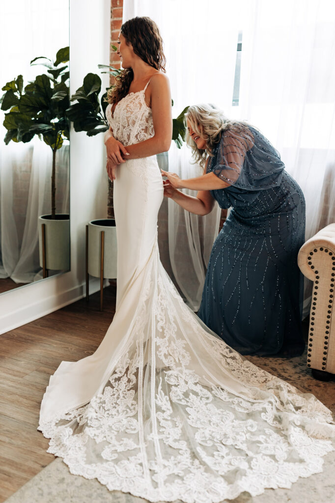 Bride getting buttoned up in her wedding dress by mom
