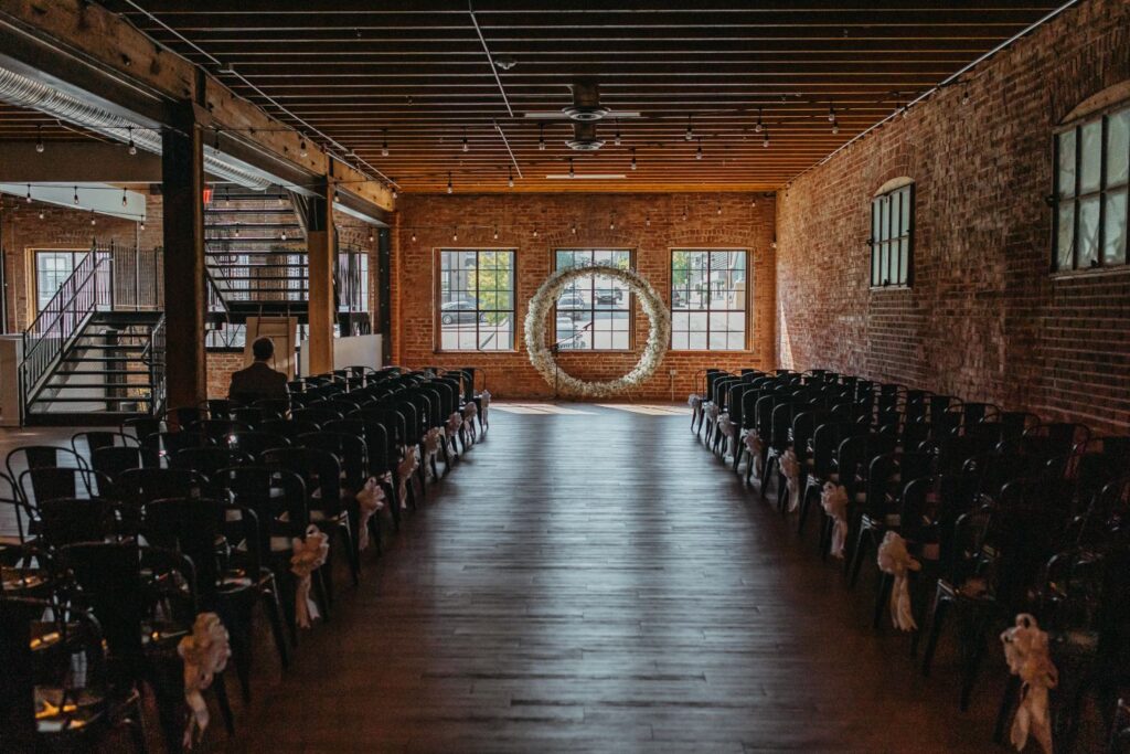 Elegant wedding ceremony setup at UNION event space in Kansas City, MO, featuring rows of chairs and a floral circular arch in front of large windows.
