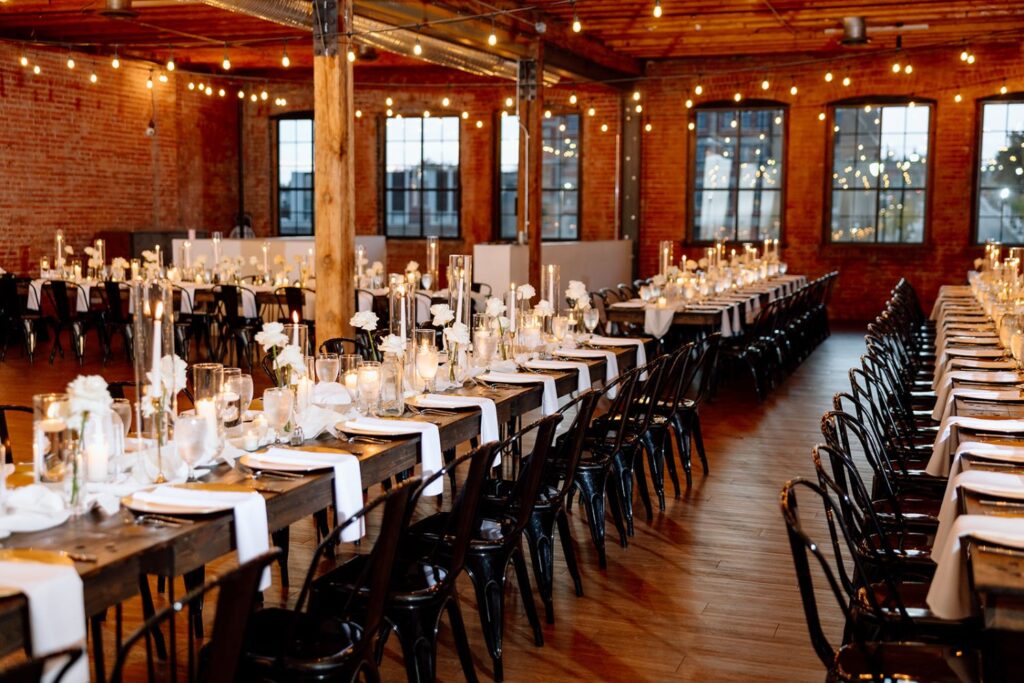 Long rows of decorated dinner tables with white linens, candles, and floral centerpieces at a wedding reception at UNION in Kansas City, MO.