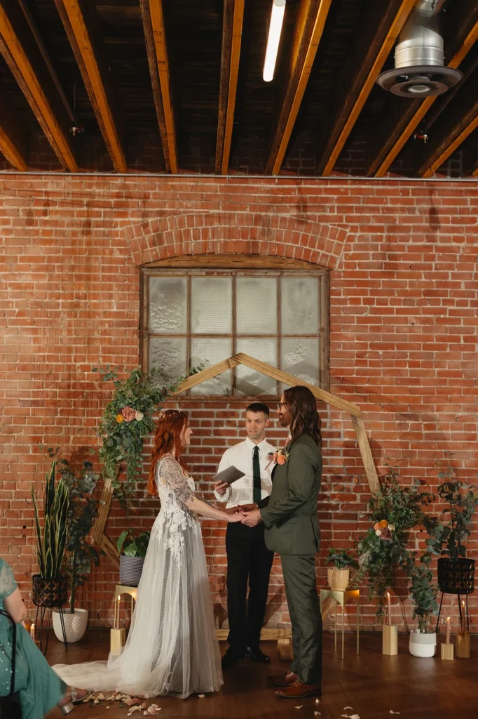 Bride and groom standing in front of a wooden hexagon arch and lots of plants for their wedding ceremony at UNION in downtown Kansas City.
